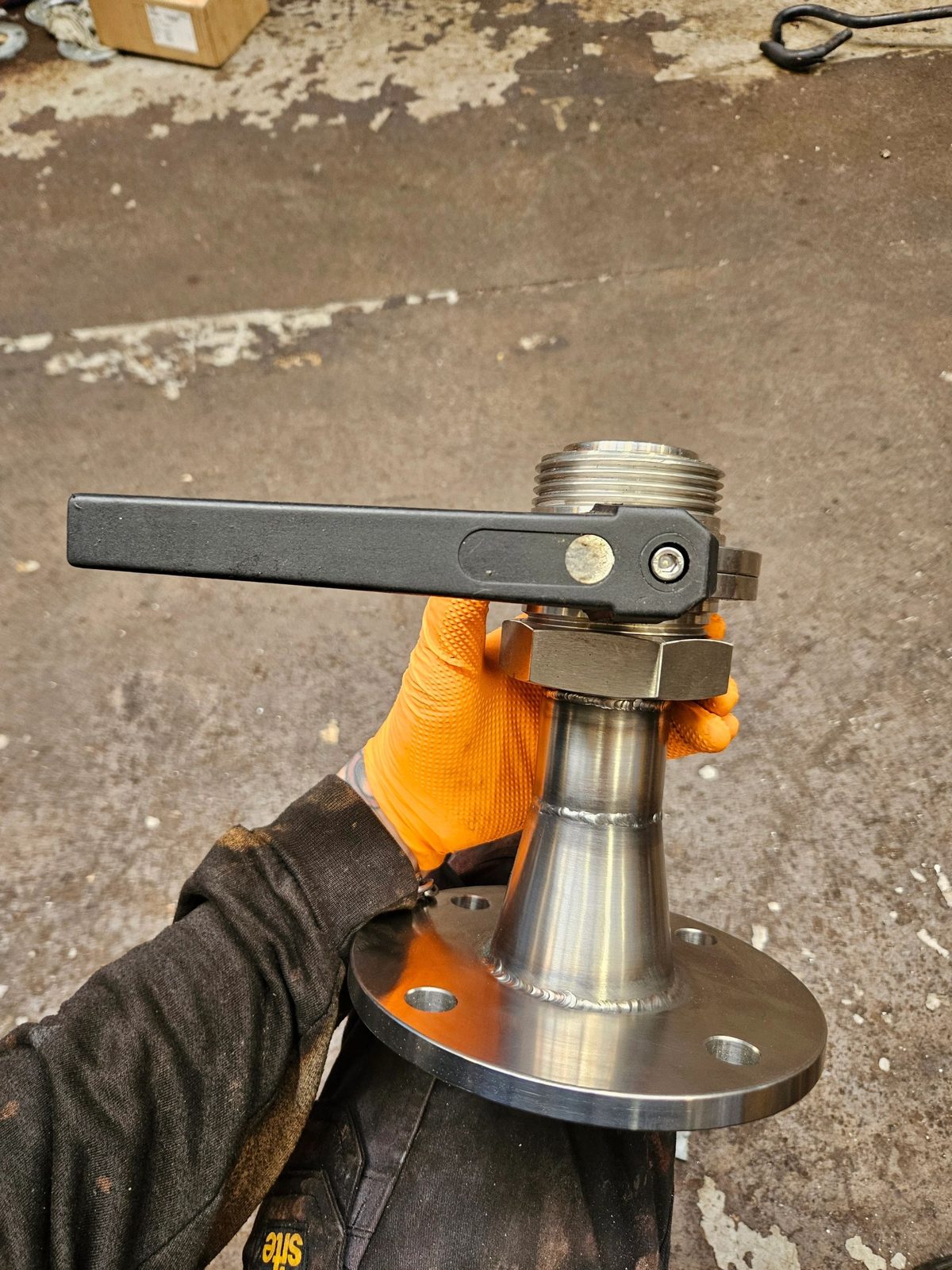 Hand holding a metallic valve with a black handle.